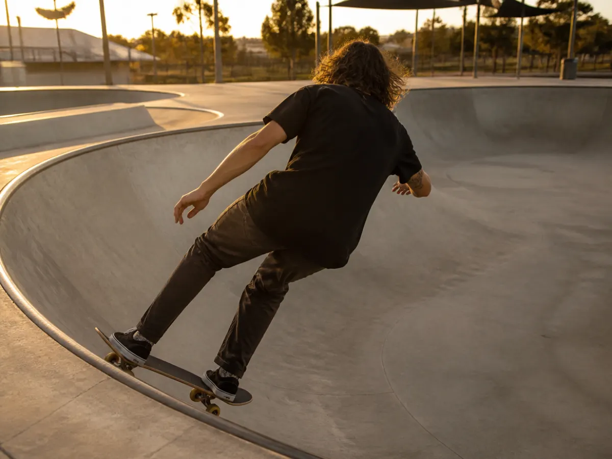 Illustration: a skateboarder carving a smooth concrete bowl at a public outdoor skatepark at golden hour